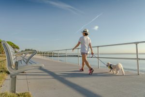 Woman walking on a sidewalk with dog, embracing the calm morning atmosphere.